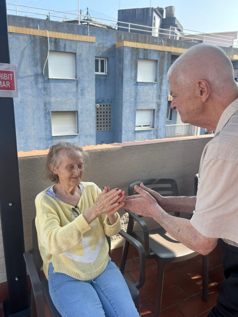 Persona mayor utilizando un dispositivo de teleasistencia en casa junto a un familiar, servicio de apoyo y seguridad para mayores – La Vostra Llar